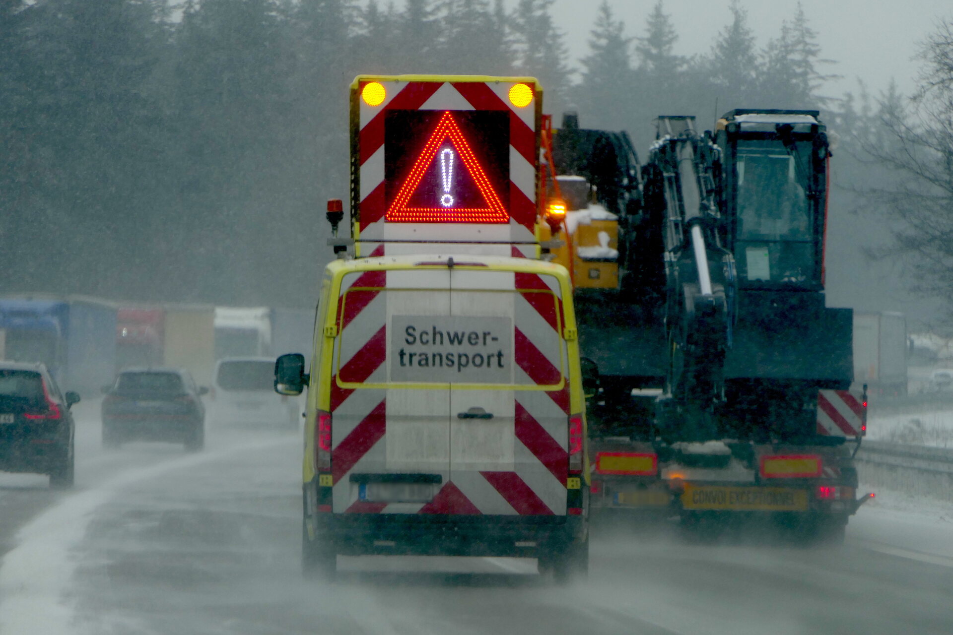 Pojazd pilotujący z tablicą zmiennej treści jadący za transportem koparki w deszczu